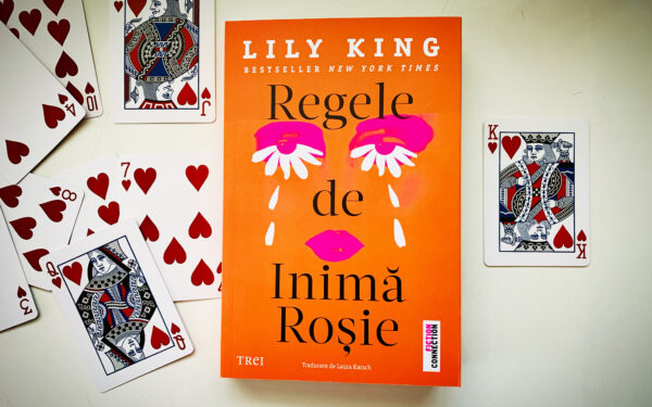 Romanul „Regele de inimă roșie” de Lily King, apărut la Editura Trei, așezat central pe o suprafață albă, înconjurat de cărți de joc de inimă roșie, evidențiind coperta portocalie cu ilustrație grafică modernă.