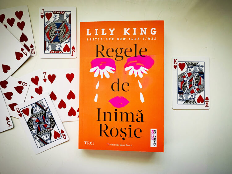 Romanul „Regele de inimă roșie” de Lily King, apărut la Editura Trei, așezat central pe o suprafață albă, înconjurat de cărți de joc de inimă roșie, evidențiind coperta portocalie cu ilustrație grafică modernă.