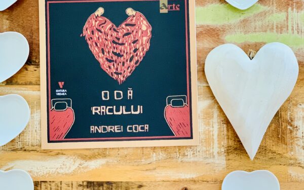 Coperta volumului „Odă Racului” de Andrei Coca, publicat la Editura Vremea, așezată pe un fundal din lemn rustic, alături de mai multe decorațiuni albe în formă de inimă.