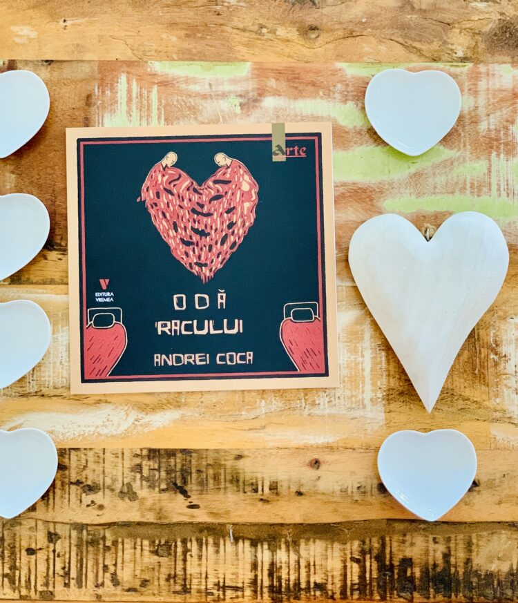Coperta volumului „Odă Racului” de Andrei Coca, publicat la Editura Vremea, așezată pe un fundal din lemn rustic, alături de mai multe decorațiuni albe în formă de inimă.