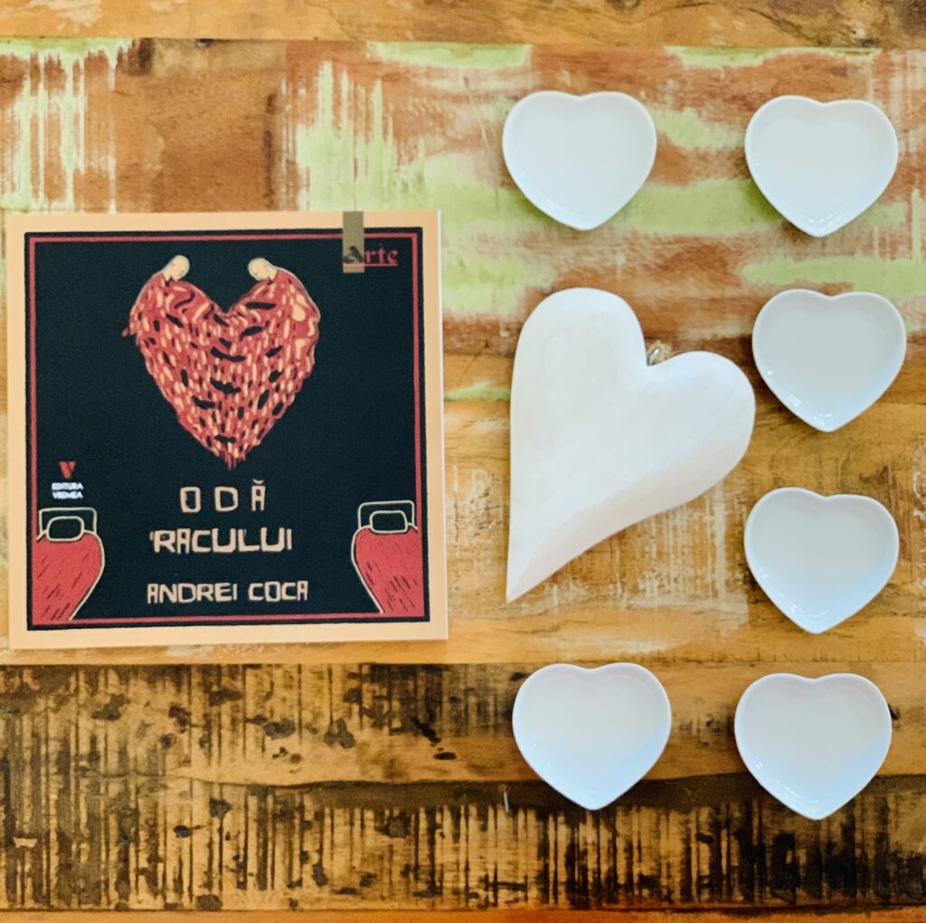 Volumul de poezii și desene „Odă Racului” de Andrei Coca, apărut la Editura Vremea, prezentat într-un decor artistic cu inimi albe pe o masă din lemn.