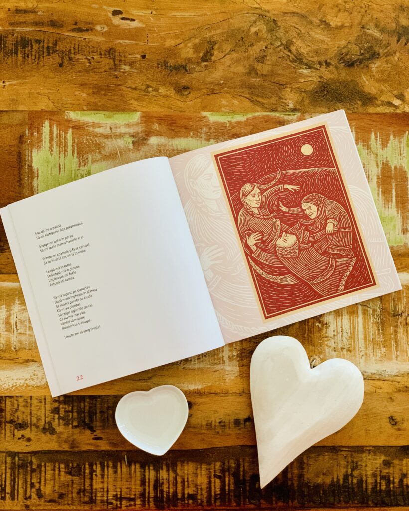 Pagini deschise din volumul „Odă Racului” de Andrei Coca, prezentând o poezie și o ilustrație roșie de tip linogravură, așezate pe o masă din lemn lângă decorațiuni în formă de inimă.