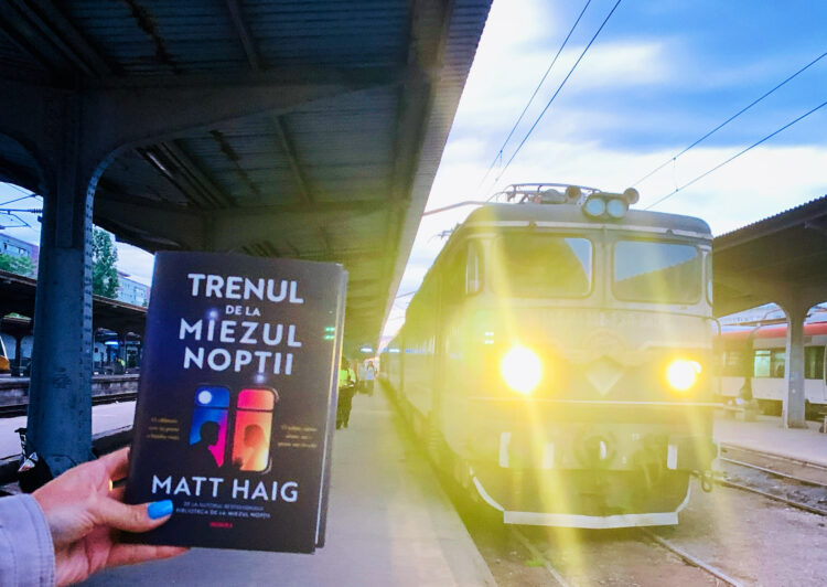 Noul roman Trenul de la miezul noptii de Matt Haig tinut in mana pe peronul garii langa o locomotiva de tren