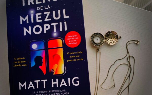 Coperta cartii Trenul de la miezul noptii de Matt Haig editia Nemira asezata pe o masa alba langa un ceas de buzunar cu lant