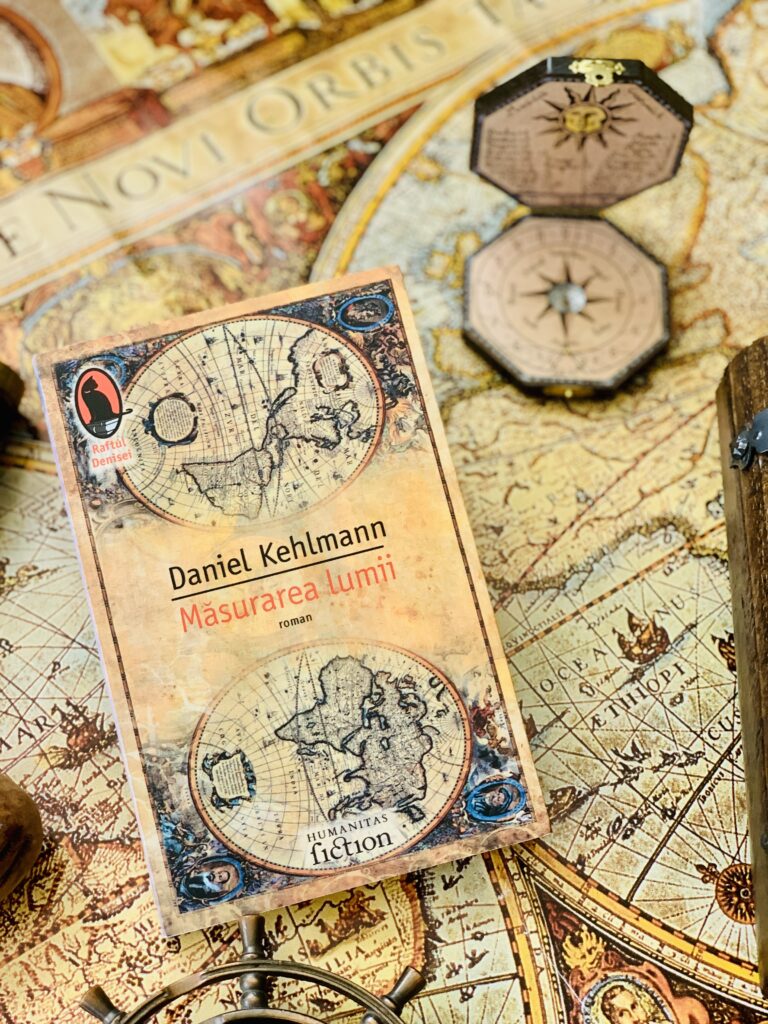 Masurarea lumii Daniel Kehlmann - cartea Humanitas Fiction asezata in prim plan pe o harta veche de epoca langa un cadran solar