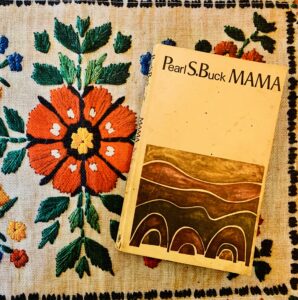 Carte veche cu romanul Mama de Pearl S. Buck așezată pe un ștergar tradițional brodat manual cu flori colorate.