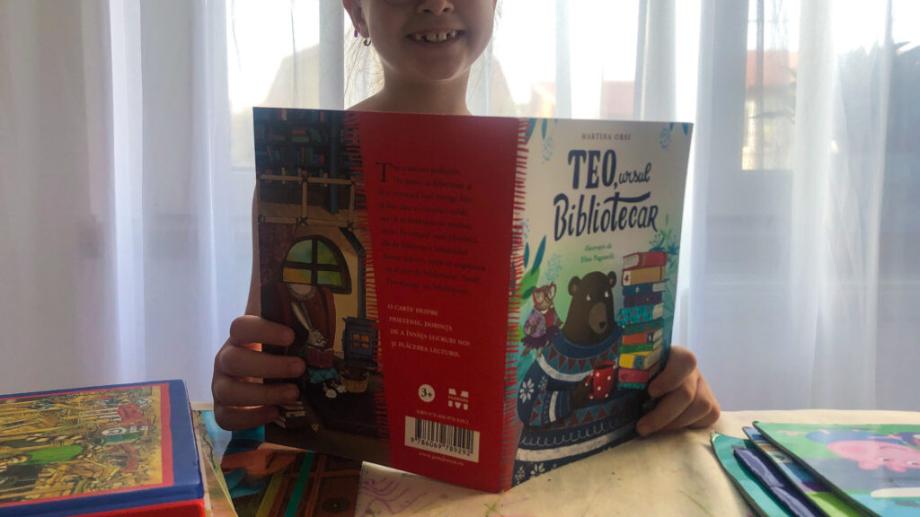 O fetita care tine in mana cartea Teo, ursul bibliotecar