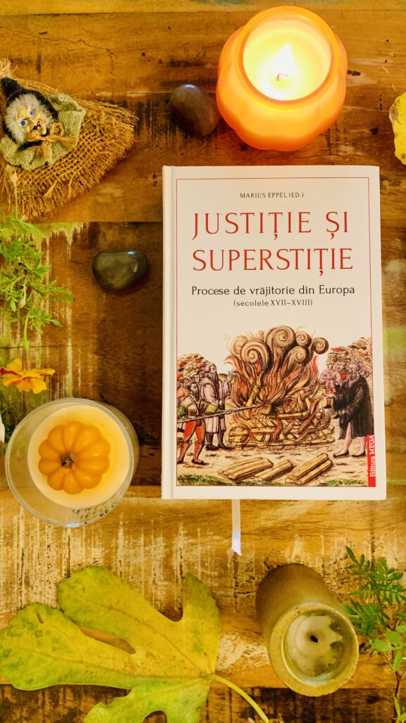 Volumul Justitie si superstitie pe o masa de lemn inconjurat de obiecte de toamna si magice